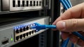A hand plugging a blue ethernet cable into a network switch with multiple ports Royalty Free Stock Photo