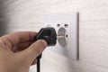 Hand plugging in an electric cord into a white plastic modern socket or european wall outlet on grey wall. Closeup of a man hand Royalty Free Stock Photo