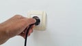 Hand plugging in an electric cord into a white plastic socket on white wall