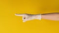 The hand is pointing finger and wear a medical glove on yellow background. Studio shooting. Royalty Free Stock Photo