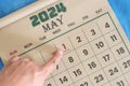 Hand pointing on May 1 2024 date on calendar flat lay in blue background. Labor day or International workers day celebration