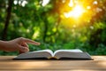 hand pointing at open book in sunlit forest setting, symbolizing knowledge and reflection. warm sunlight enhances serene Royalty Free Stock Photo