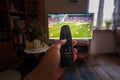 A hand pointing remote control at tv or television set with soccer or football match indoors, point of view, wide angle with Royalty Free Stock Photo