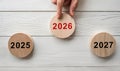 Hand Pointing to 2026 Wooden Disc Between Years 2025 and 2027 on White Table Royalty Free Stock Photo