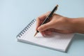 Hand poised with pen, ready to write on lined notepad, black pen visible