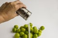 Hand is pour salt spills from metal salt shaker on green plums on the white background Royalty Free Stock Photo