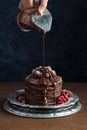 Hand Pouring Chocolate Sauce over Pancakes with Berries