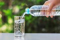 hand pouring drinking water into glass form bottle