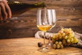 Hand is pouring dry white wine from a bottle into a glass on a wooden table. Concept of viticulture and winemaking Royalty Free Stock Photo