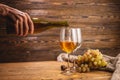 Hand is pouring dry white wine from a bottle into a glass on a wooden table. Concept of viticulture and winemaking Royalty Free Stock Photo