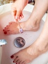 Hand pouring epsom salt from small wooden spoon and female feet in foot spa marble basin