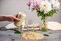 Hand is pouring into a glass of natural vegetable oatmeal milk. Alternative vegetarian drink for a healthy diet