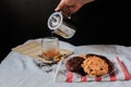 Hand pouring hot tea into glass with almond milk cookie and dark chocolate cookie on white table black background.