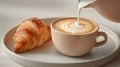 hand pouring milk into fresh espresso cup beside croissant Royalty Free Stock Photo