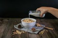 Hand pouring milk into granola bowl on wooden table with dark background. Healthy cereal and fiber food. Royalty Free Stock Photo