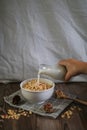 Hand pouring milk into granola bowl on wooden table with dark background. Healthy cereal and fiber food. Royalty Free Stock Photo