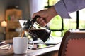 A hand pouring steaming coffee in to a cup on a work desk when work from home Royalty Free Stock Photo