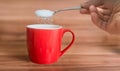 Hand is pouring sugar to red cup of tea. Unhealthy eating concept Royalty Free Stock Photo