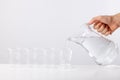 Hand pouring water from glass jug to glass against white background