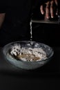 Hand dropping water over a bowl with flour on a black background Royalty Free Stock Photo