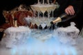 a hand pours champagne from a bottle into glasses steaming with dry ice on a dark background