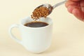 Hand pours granulated coffee from spoon in a coffee cup