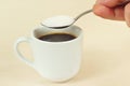 Hand pours sugar from spoon in a coffee cup