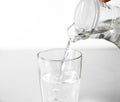 Hand pours water into a glass glass Cup from a glass jug. Close up. Isolated on white background Royalty Free Stock Photo