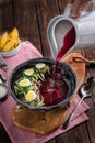 Hand pours from a white jug ?old beetroot soup with eggs. Baked potatoes, souce, pink tablecloth on the rustic wooden background. Royalty Free Stock Photo