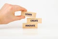 Hand presents three wooden blocks stacked vertically with the words learn create innovate clearly displayed, emphasizing