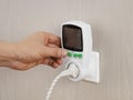 Hand presses button in wattmeter on wall, for measuring electricity costs in device
