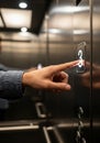 A hand presses a lit elevator button labeled \