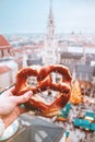 Hand with pretzel on the background of the panorama of Munich square, town hall, Christmas fair. Germany in winter.