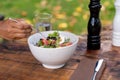 Hand pricking with a fork a salad with mixed green leaves, eggs, black olives and tomato on a wooden rustic table with a glass of Royalty Free Stock Photo