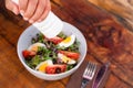 Hand pricking with a fork a salad with mixed green leaves, eggs, black olives and tomato on a wooden rustic table with a glass of Royalty Free Stock Photo