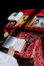 Hand of priest holds opened Holy Bible on the lectern near cross and icons