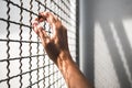 Hand of prisoner holding rustic metal fence with pattern shadow, criminal locked in jail