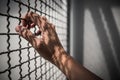 Hand of prisoner holding rustic metal fence with pattern shadow, criminal locked in jail
