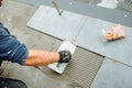 hand of professional construction worker, tiler laying adhesive and placing ceramic tiles on balcony floor. Royalty Free Stock Photo