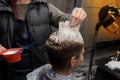 The hand of a professional hairdresser in the process of dyeing the client\'s hair white in a barbershop