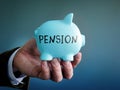 Hand proposes piggy bank with sign pension as symbol of savings for retirement