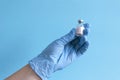 Hand in protective blue gloves hold medicine bottle of vaccine on blue background. Concept of vaccination and healthcare Royalty Free Stock Photo