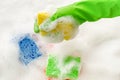 Hand in protective glove holding a soapy sponge on foam background. Royalty Free Stock Photo