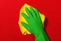 Hand in a protective green glove with a yellow napkin on a red colored background. The concept of cleaning, home care Royalty Free Stock Photo