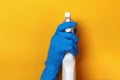 A hand in a protective latex glove holds a spray bottle on a yellow colored background Royalty Free Stock Photo