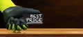 Gloved Hand Holding a Best Price Sign on a Wooden Workbench Royalty Free Stock Photo
