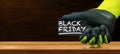 Gloved Hand Holding a Black Friday Sign on a Wooden Workbench