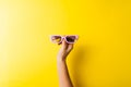 Hand with purple sunglasses on yellow background. Minimal concept of trendy colourful glasses. 3d movie theatre