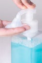 Hand pushing foam bubbles from plastic transparent bottle dispenser  with blue liquid soap macro Royalty Free Stock Photo