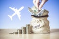 Hand put coin in Bag with US dollar bills, coins Stack on table, blur background with silhouette of the plane. Concept of money Royalty Free Stock Photo